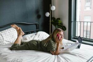 woman laying on a bed and looking at papers while on the phone