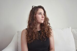 A woman looking off to the right on a couch alone, daydreaming